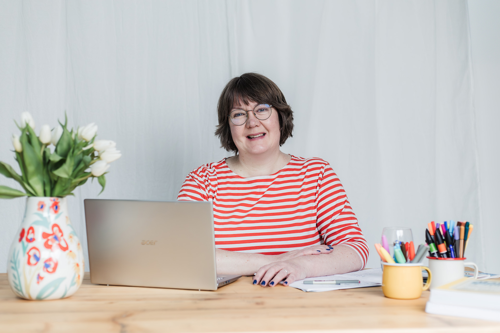 Jane Wilson at desk with laptop, flowers and pens