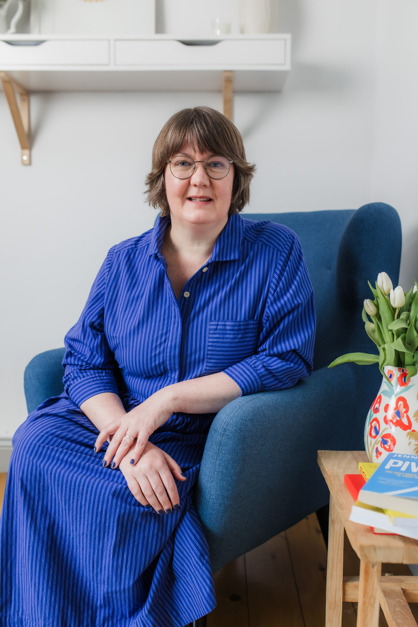 woman in blue dress and glasses smiles at the camera